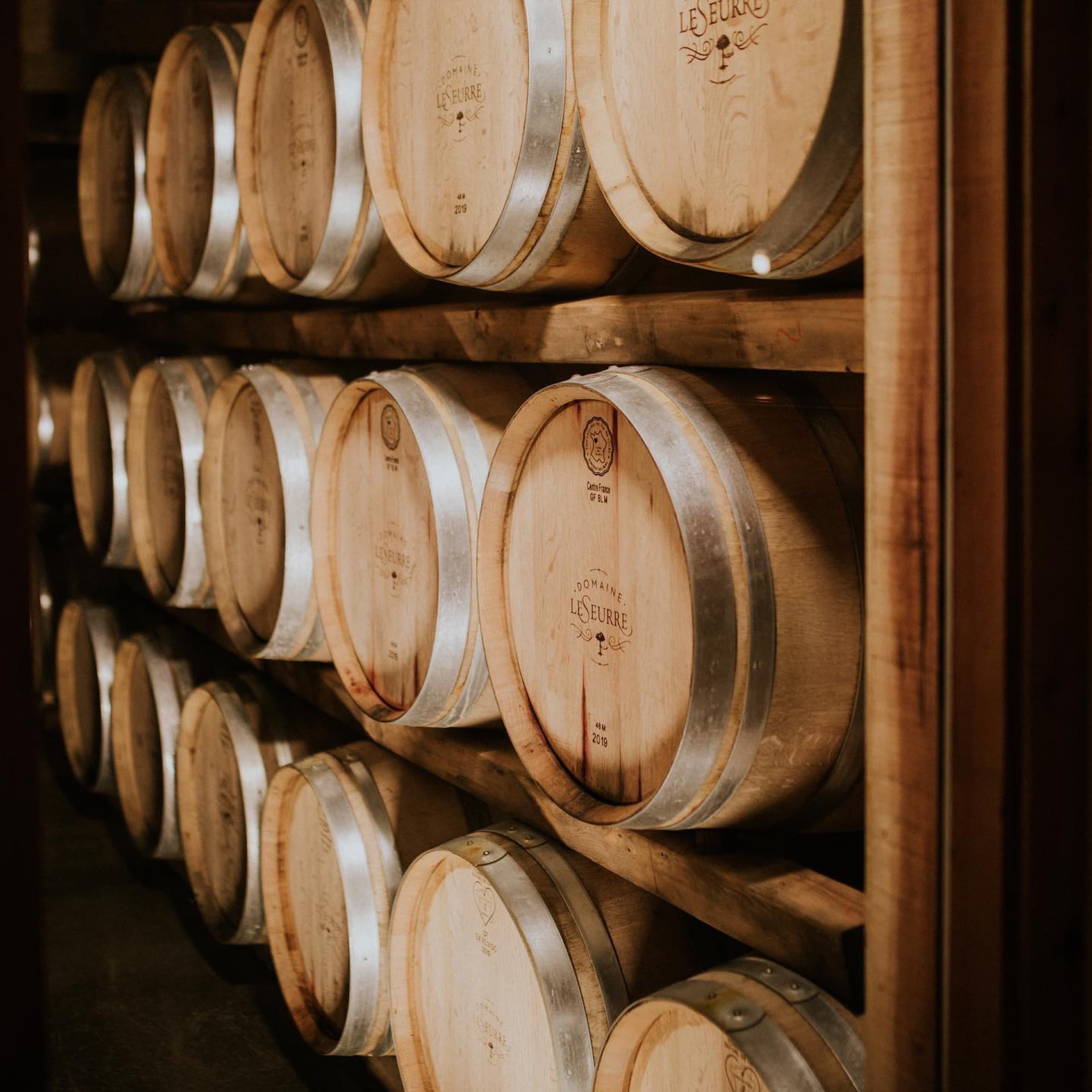 Rows of Domaine LeSeurre oak barrels resting in the cellar.