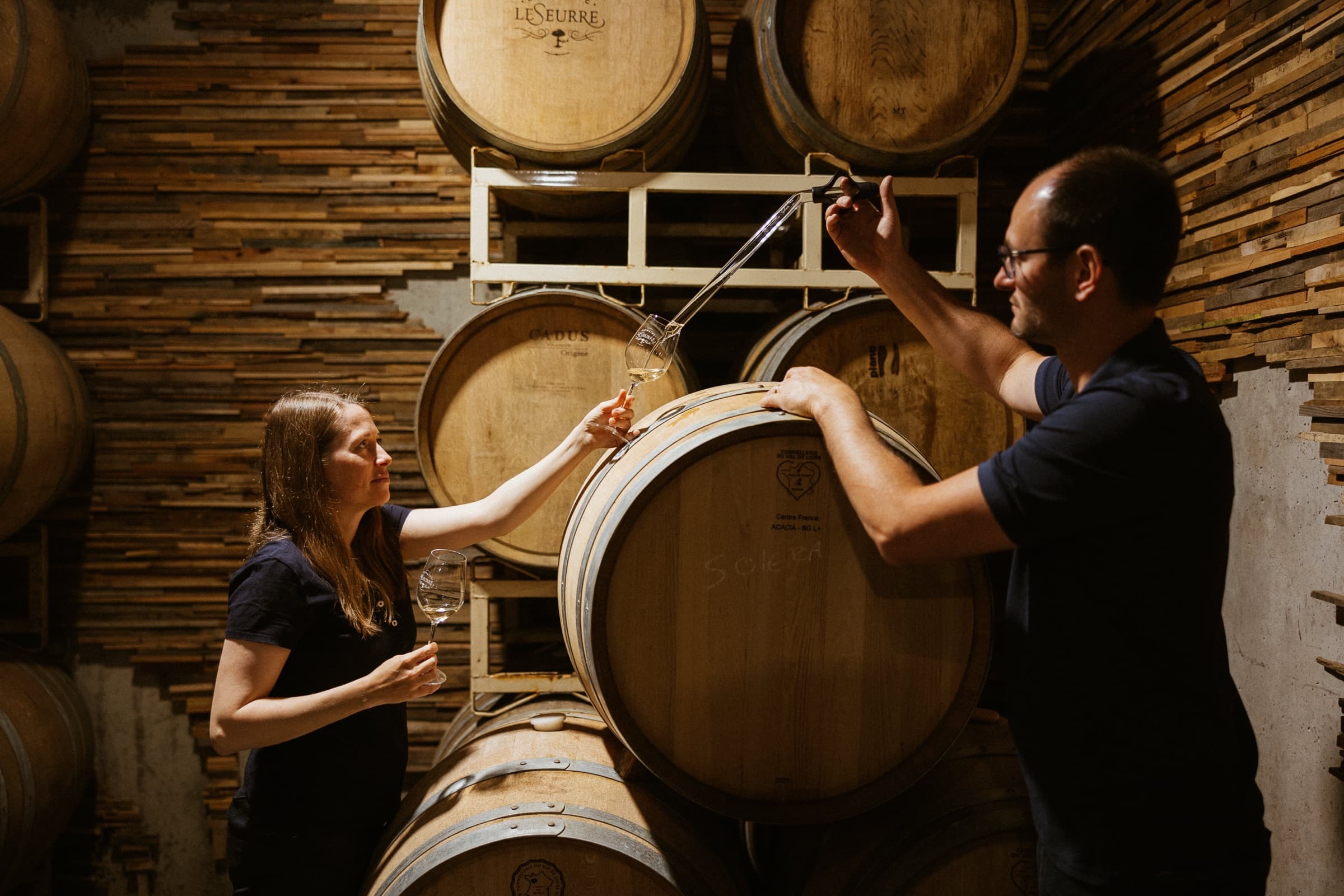 Céline and Sébastien LeSeurre drawing wine from an oak barrel in the cellar.